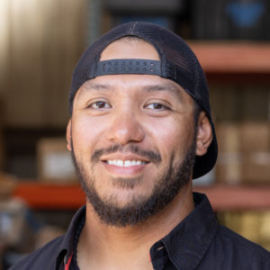 A man in a black shirt smiling in a warehouse.