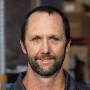 A man with a beard standing in a warehouse.