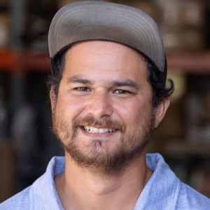 A man with a hat smiling in a warehouse.