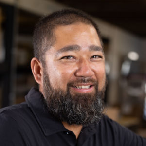 A man with a beard smiling in a black shirt.