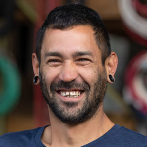 A man with a beard smiling in front of a bunch of wires.