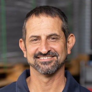 A man with a beard smiling in a warehouse.