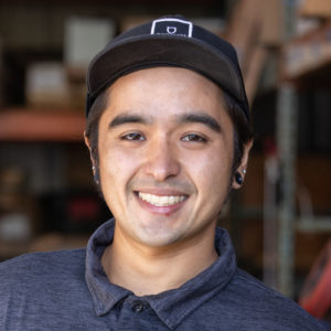 A man in a black shirt smiling in a warehouse.