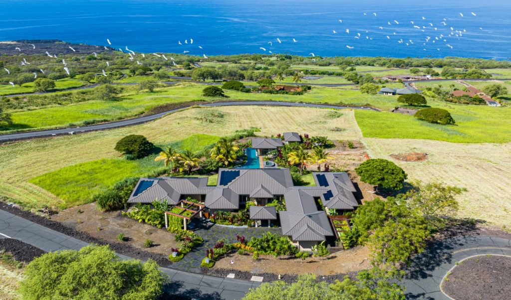 An aerial view of a home with rooftop solar panels on a hill overlooking the ocean.