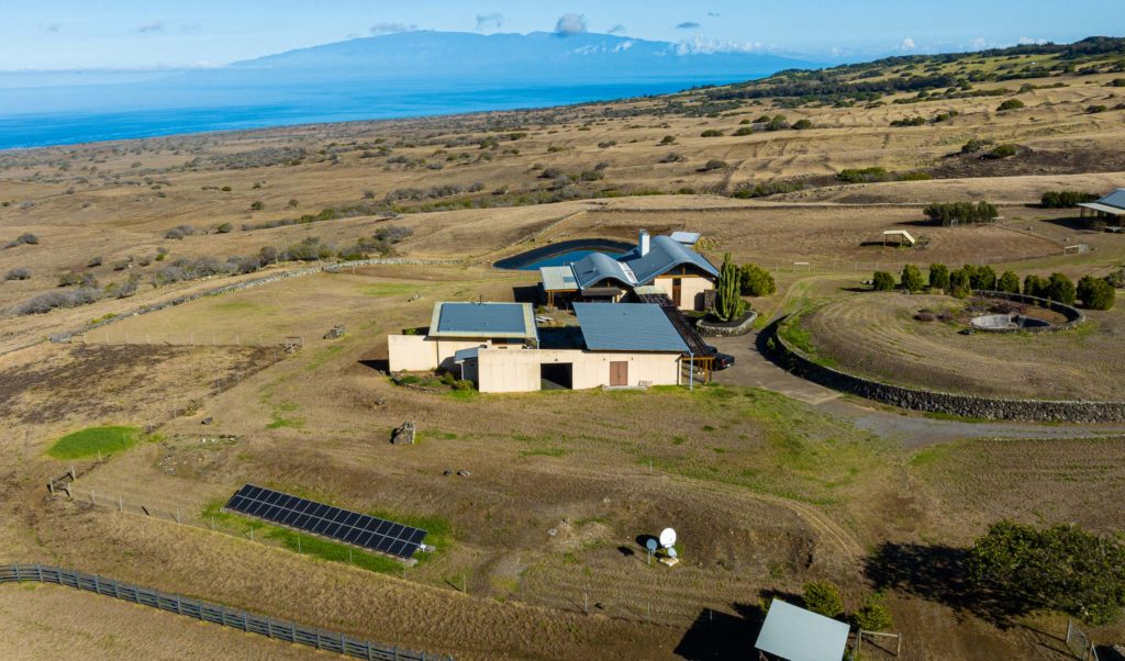 An aerial view of a house with solar panels and a view of the ocean.